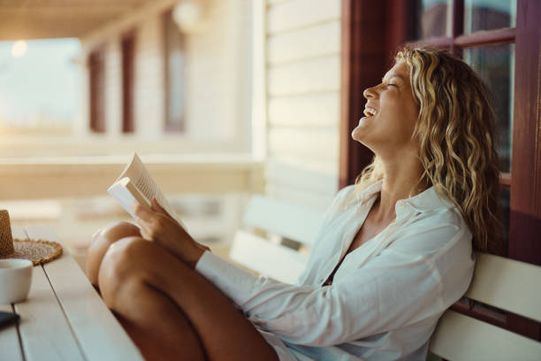 istock Cheerful woman reading a book on a bench at patio. 1484360595