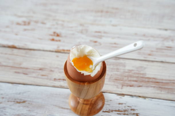istock Soft-boiled egg in wooden egg cup showing runny yellow yolk with matching white ceramic spoon. 1484363448