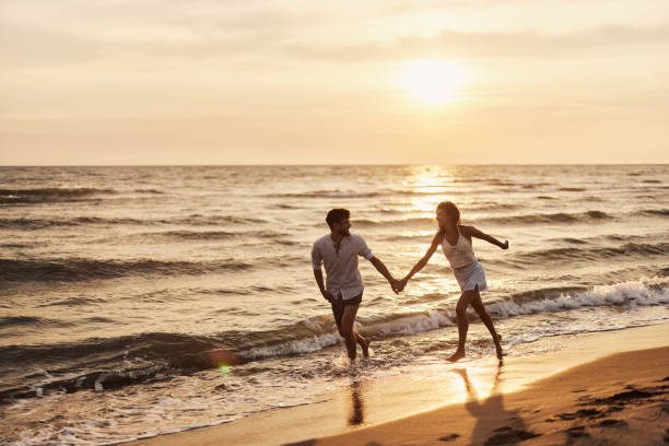 istock Young cheerful couple running on the beach at sunset. 1484370670