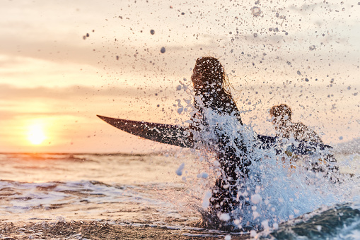 Couple of surfers having fun while rushing into sea at sunset. Copy space.