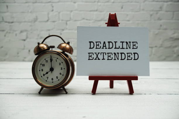 istock Deadline Extended text and alarm clock on white brick wall and wooden background 1484384267