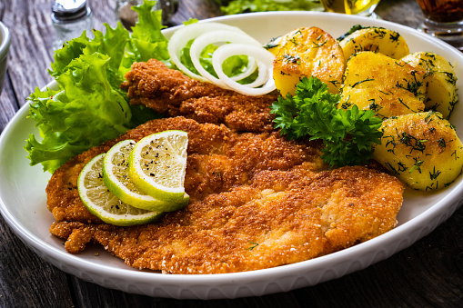 Breaded fried pork chop with fried potatoes and lime on wooden table