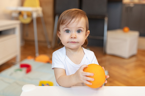 Adorable one year old child playing with orange, shallow depth of field