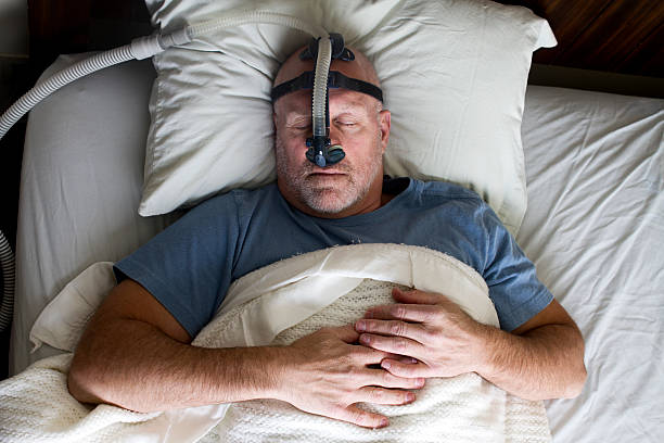 Man Sleeping in Bed with Sleep Apnea Mask Photo of a man sleeping while wearing a CPAP mask. sleep apnea photos stock pictures, royalty-free photos & images