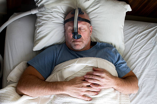 Homem a dormir na cama com Máscara de apneia do sono - fotografia de stock