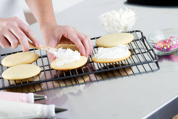 Spreading Frosting on a Cookie A woman decorating sugar cookies with frosting. white sugar cookie stock pictures, royalty-free photos & images