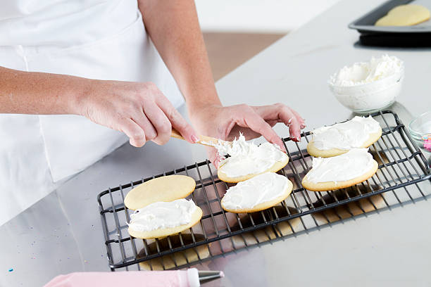 Spreading Frosting on a Cookie A woman decorating sugar cookies with frosting. round sugar cookie stock pictures, royalty-free photos & images