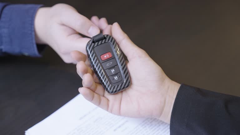 Man's hand wearing business suit signing a vehicle lease agreement before salesman delivering him the car key at a car dealer.