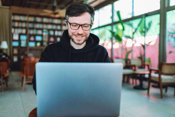 istock Young adult smiling freelancer man working at cafe using laptop 1484420686