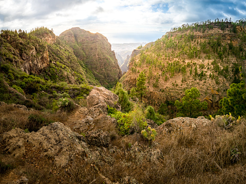 A thrilling panoramic view of the Barranco del Infierno ravine, Hell's Gorge, from above with sunlight illuminating the dangerous terrain leading down to Adeje coast of the Atlantic Ocean on Tenerife.
