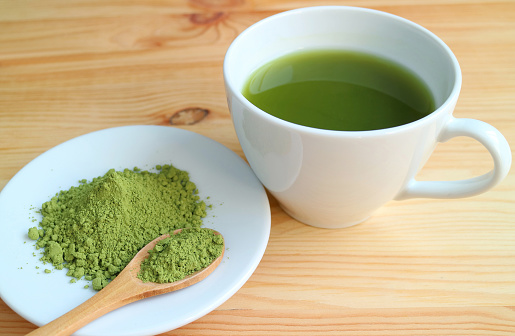 Cup of Hot Matcha Green Tea with a Plate of Matcha Tea Powder on Wooden Table