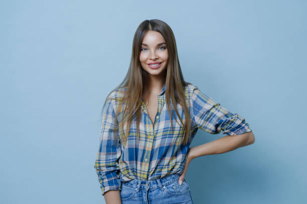istock Charming pretty millennial lady keeps hand on figure, stands confident and smiles cheerfully, wears checkered shirt and jeans stands in casual posture happy to meet with friend enjoys pleasant talk 1484446050