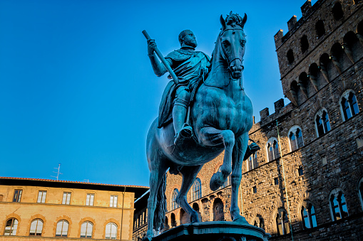Florence, Italy - August 13, 2016: The Equestrian Monument of Cosimo I is a bronze statue located in the Piazza della Signoria in Florence, Italy. The statue depicts Cosimo I de' Medici, the first Grand Duke of Tuscany, on horseback, dressed in full armor and holding a baton.\nThe statue was created by the renowned Italian sculptor Giambologna in the late 16th century. It stands atop a pedestal made of white Carrara marble, which features reliefs depicting scenes from Cosimo's life and the allegories of Justice and Military Virtue.\nThe statue itself is a masterpiece of Renaissance art, with its dynamic composition and attention to detail. Cosimo's horse is shown rearing up on its hind legs, with its front legs lifted as if in motion. The horse's muscles and veins are sculpted with great precision, giving it a sense of strength and vitality. Cosimo, too, is shown in a commanding pose, with his head held high and his arm outstretched.\nThe Equestrian Monument of Cosimo I is considered one of the finest equestrian statues in the world and a testament to the skill and artistry of Giambologna. It remains an iconic symbol of Florence and an important landmark in the city's historic center.