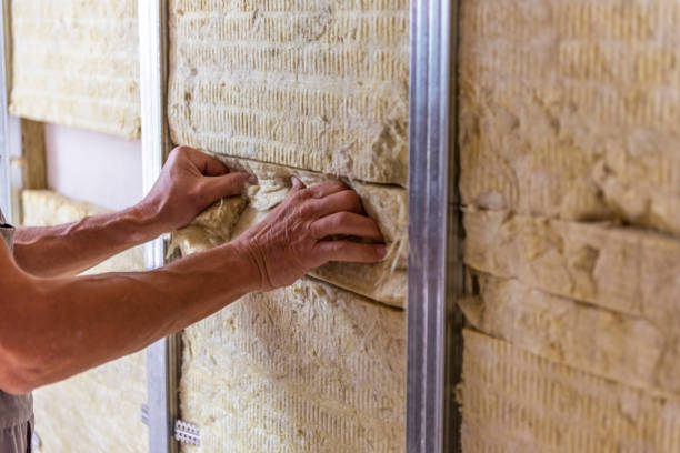 Worker insulating a room wall with mineral rock wool thermal insulation.