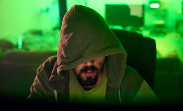 Photo of Computer hacker, hoodie or neon man hacking database software, online server or password phishing. Green ransomware developer, cybersecurity programming or hidden night programmer coding malware code