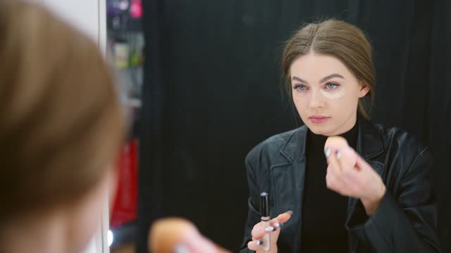 Woman applying concealer to under-eye circles in a backstage