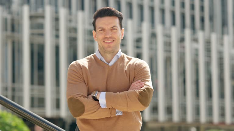 Happy businessman smiling at the camera with arms crossed outdoors