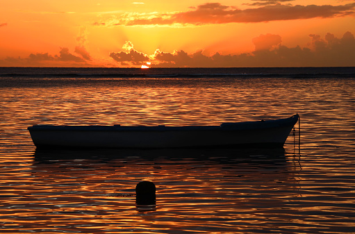 Albion, Mauritius - April 18, 2023: Vibrant colors during sunset at the Indian Ocean close the public beach with a fisherman boat in Albion in the West of Mauritius.