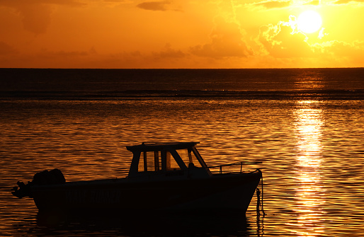Albion, Mauritius - April 18, 2023: Vibrant colors during sunset at the Indian Ocean close the public beach with a fisherman boat in Albion in the West of Mauritius.