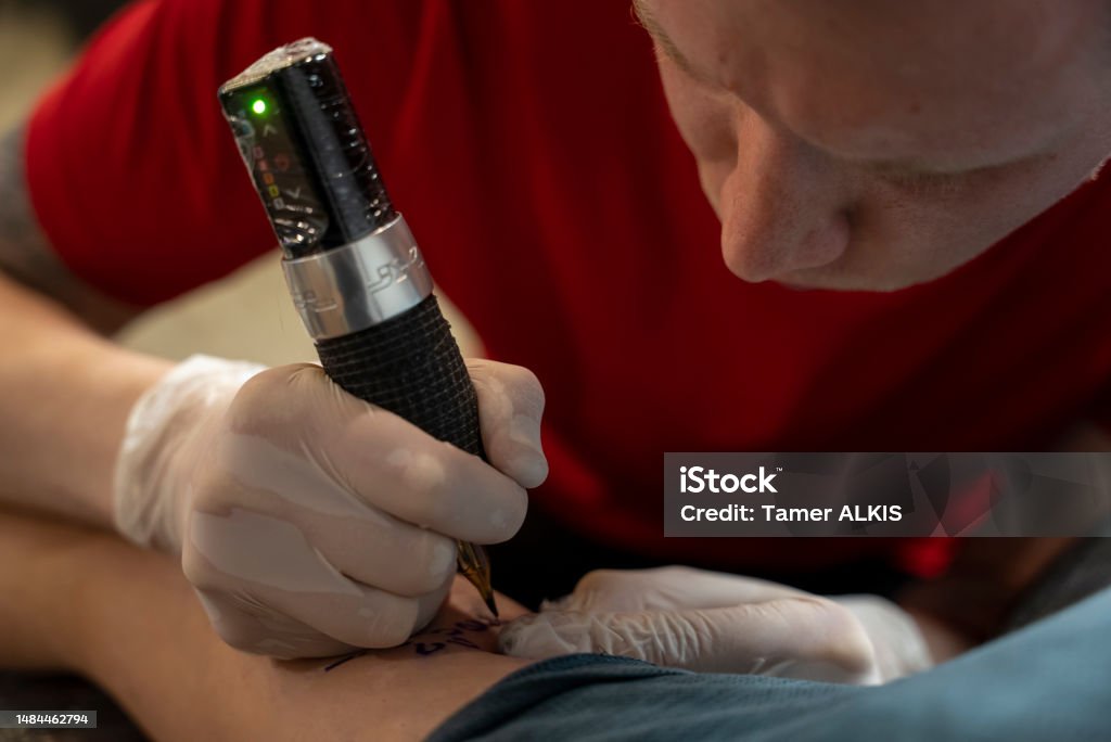 young tattoo artist doing tattoos to young man arm’s 25-29 Years Stock Photo young tattoo artist doing tattoos to young man arm’s 25-29 Years Stock Photo