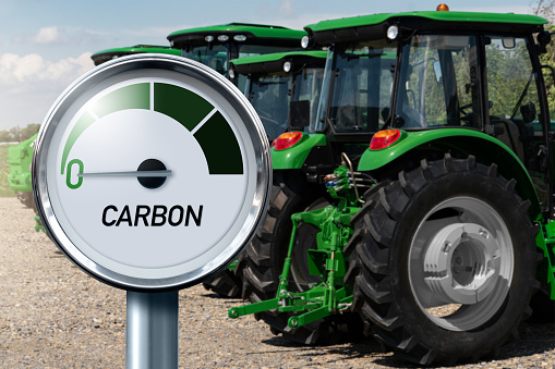 Gauge with inscription CARBON and arrow points to zero on a background of agricultural tractors