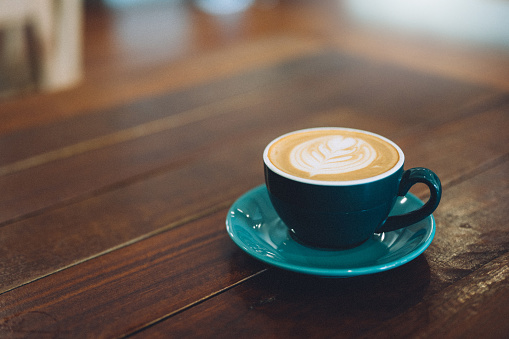 A cup of cappuccino with latte art on a wooden table in the morning light.