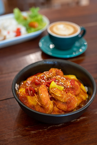 Fried sticky shrimps with garlic, chilli, and pineapple served with rice close-up in a bowl at wooden table.