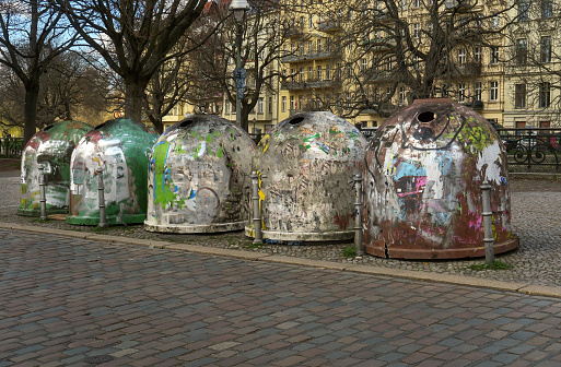 trash collection bins for recyclables and other garbage, lined up on a street in the Mitte section of Berlin, Germany and covered with graffiti and stickers