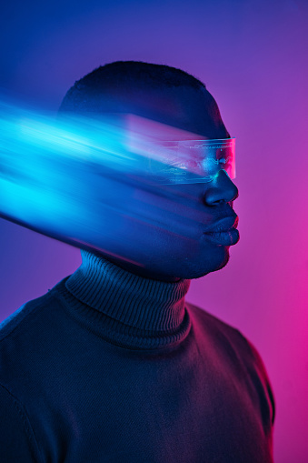 A blurred side view of an African-American man's head wearing wrap-around smart glasses and a sweater against a gradient purple background