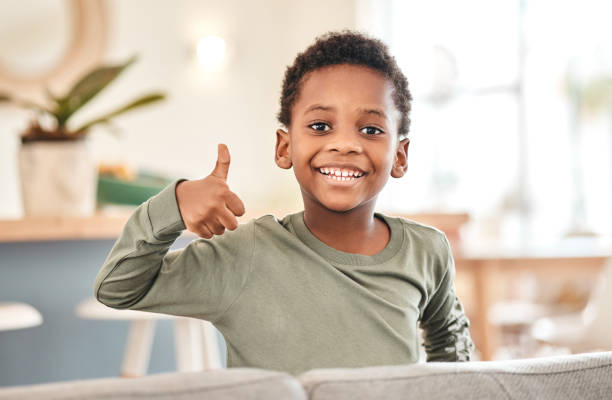 自宅のソファで親指を立てる愛らしい少年のポートレート - thumbs up child success winning ストックフォトと画像