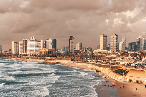 Tel Aviv Cityscape illuminated from warm late afternoon sunset light. View towards the Charles Clore Beach at the Tel Aviv Waterfront. Tel Aviv Modern Skyscraper Skyline in the background under moody cloudy skyscape. Tel Aviv, Israel, Middle East