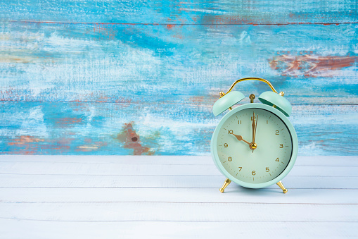 Green vintage alarm clock on a white shelf and blue wooden background.