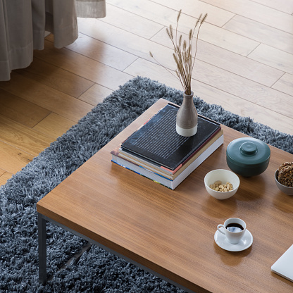 Top view on wooden coffee table with decorations, books, vase, bowls and white cup of coffee