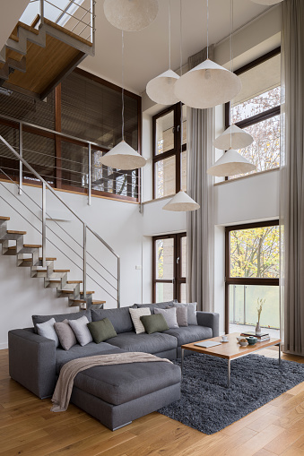 Stylish living room with big sofa, many windows and stairs in amazing two-story apartment