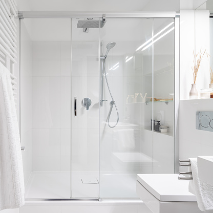 Spacious shower behind glass sliding doors in simple bathroom with white tiles