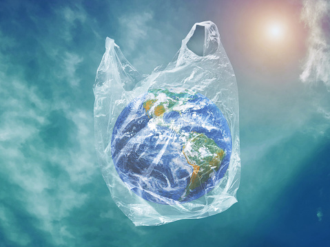 Little planet earth globe in plastic bag on the sky background./Ecology Concept/Pollution problem concept. /Global warming Concept. Earth by NASA