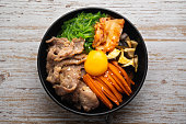 Kimchi fried rice with fried brisket and wakame seaweed and raw egg in black bowl on wooden table,(bibimbap).