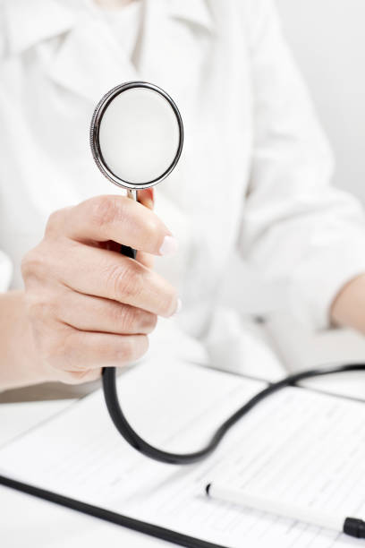 Front view of a happy young white male nurse holding a stethoscope and pointing it at camera at the hospital. The male nurse is looking at camera. Predominant color is blue.