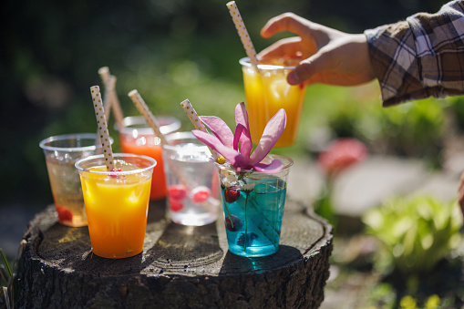 Teenager taking recyclable transparent PET (polyethylene terephthalate) cups with colorful juice and soft drinks from a tree stump.
Photographed outdoors with shallow depth of focus.
Canon R5