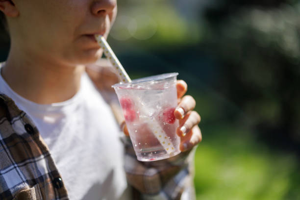 Teenager holding recyclable transparent PET (polyethylene terephthalate) cups with water and fruits drink.\nPhotographed outdoors with shallow depth of focus.\nCanon R5
