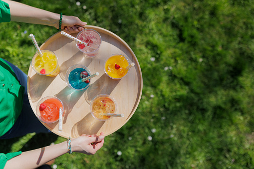 Woman carrying recyclable transparent PET (polyethylene terephthalate) cups with colorful juice and soft drinks on a wooden tray.
Photographed outdoors with shallow depth of focus.
Canon R5