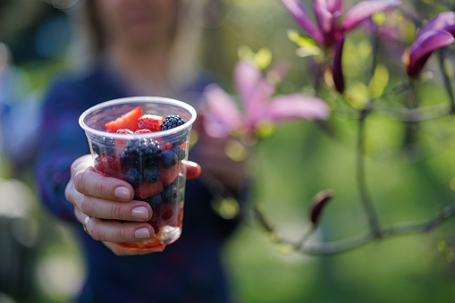 Woman holding a recyclable transparent PET (polyethylene terephthalate) cup with fresh fruit pieces.
Photographed outdoors with shallow depth of focus.
Canon R5