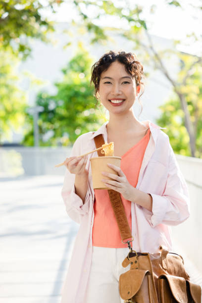Young Asian female tourists walking happily eating noodles in a tourist town. stock photo