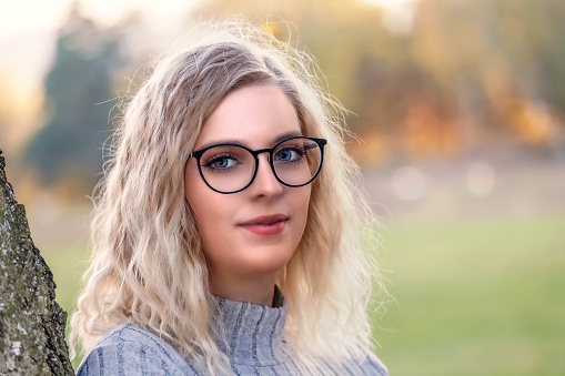 Attractive young blond woman in glasses is posing outdoors Horizontally.