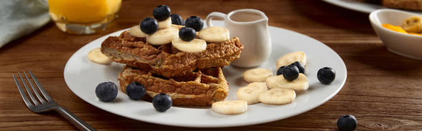 Oatmeal Belgian waffles topped with banana and blueberry on rustic wooden table