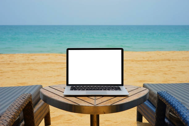 istock Laptop with blank screen for creative design on the table nearby sea and beach background. Computer notebook with monitor clipping path for present landing page design. Laptop computer mock up template 1484501558