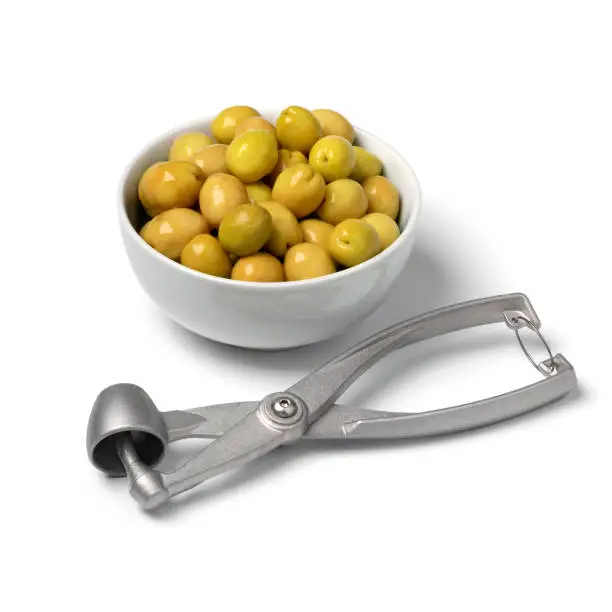 Bowl with green Turkish olives close up  and a metal olive pitter and pitted olive in front isolated on white background