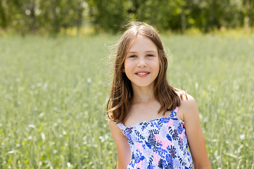 A happy girl is walking in a meadow during a summer day and looking at camera.
