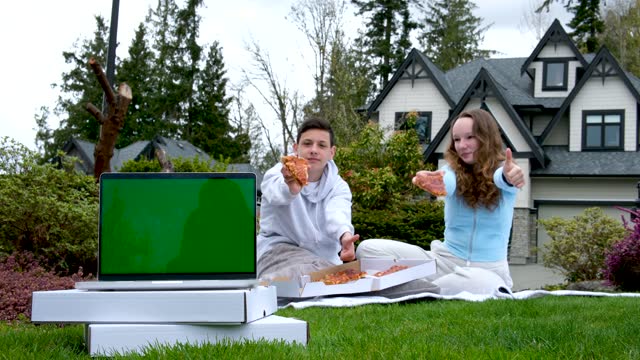 teens show pizza slices thumbs up pizza delivery youth people sitting on picnic eating pizza in background in foreground laptop with blank screen stands on white boxes with delivery summer marketing