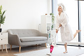 Lady after shower hoovering studio room with stick vacuum